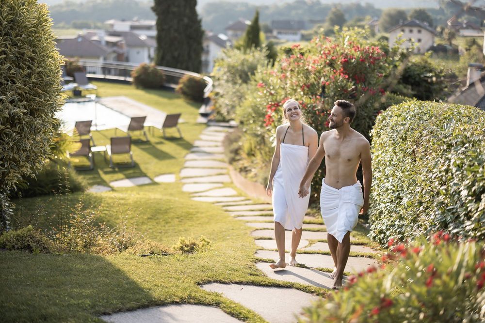 Coppia che cammina felice con asciugamani in un giardino soleggiato vicino a una piscina. Coppia che cammina felice con asciugamani in un giardino soleggiato vicino a una piscina.